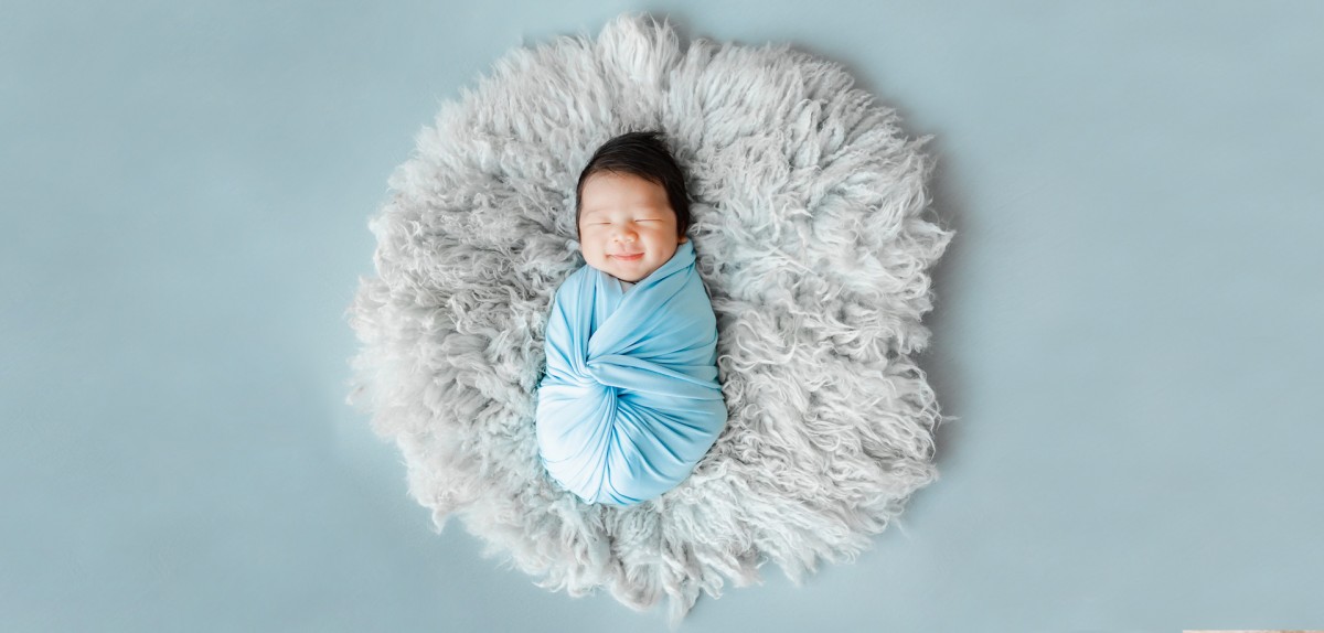 Dairy Products for All Lifestages - A baby wrapped in a light blue blanket lies on a fluffy, circular, white rug against a light blue background. The logo 'ABLE-LAC' appears beneath the baby, emphasizing Able Dairies' commitment to producing high-quality dairy products for infant nutrition.